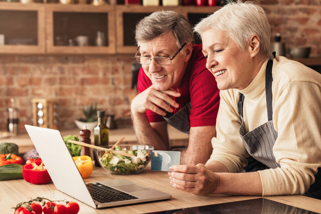 Freshop - eCommerce for Grocery & Specialty Retail Happy seniors ordering Groceries online on laptop and credit card at kitchen